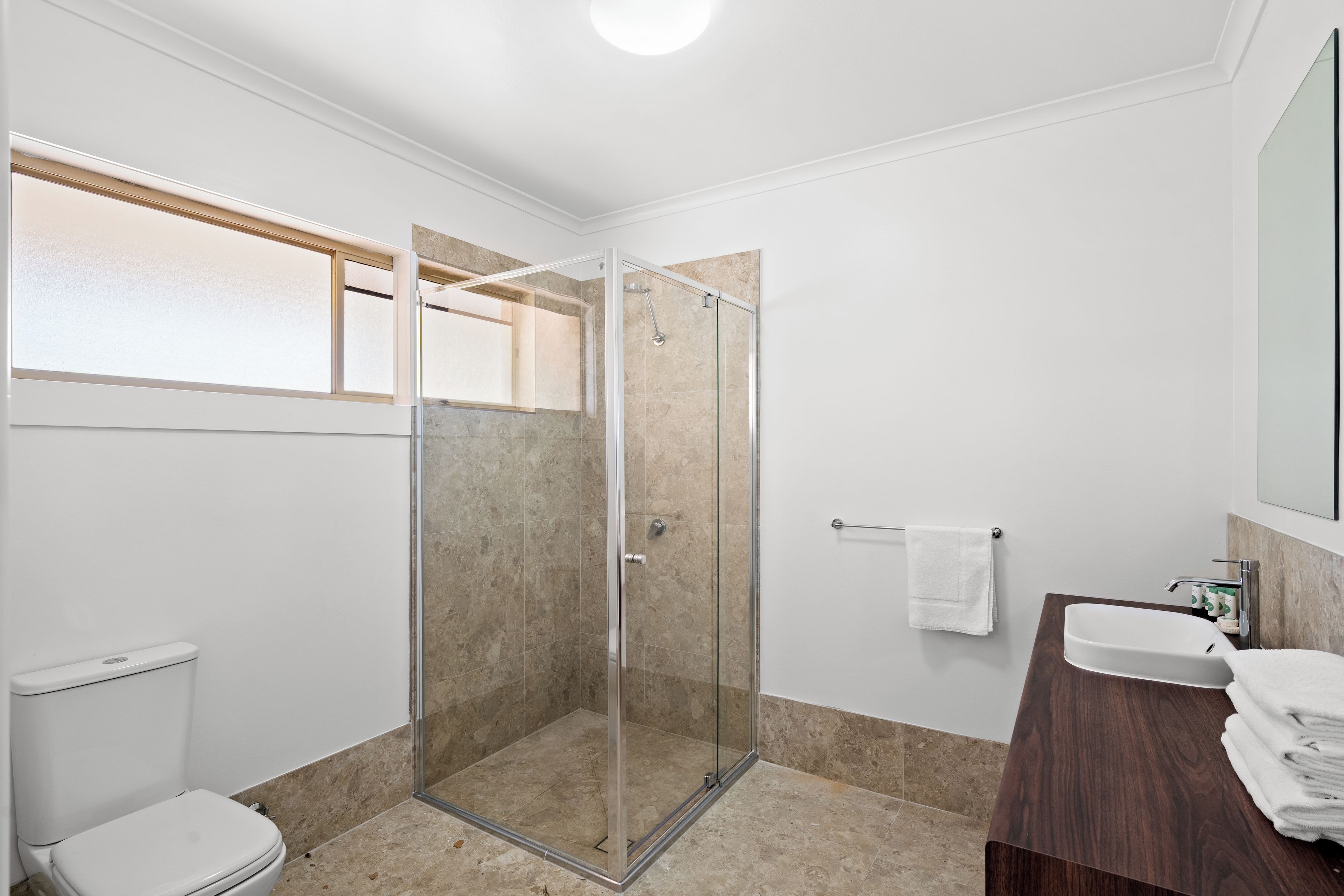 A modern bathroom with a glass-enclosed shower, a white toilet, and a wooden vanity with a mirror.