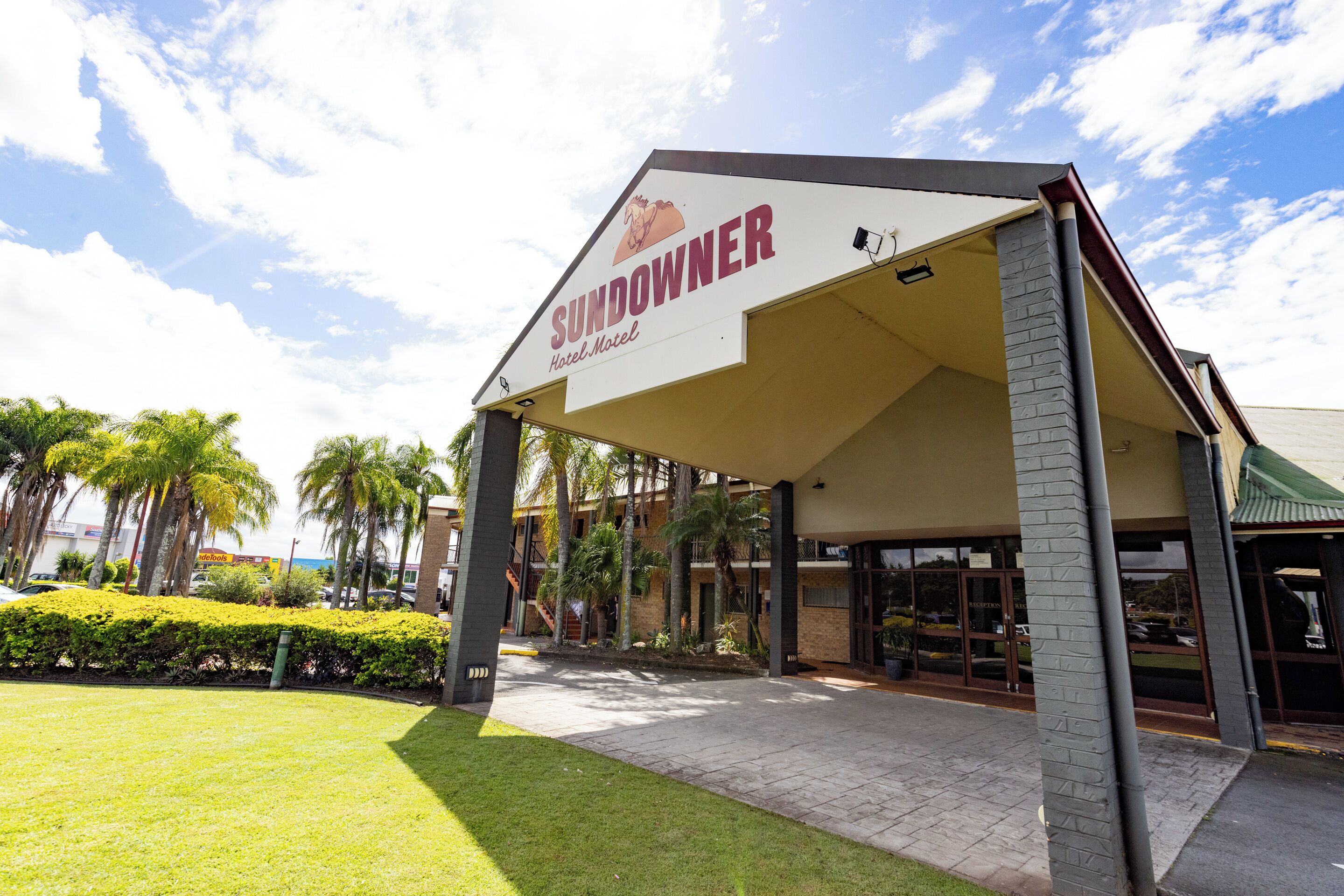 A hotel named 'Sundowner' with a covered entrance, palm trees, and a clear sky.