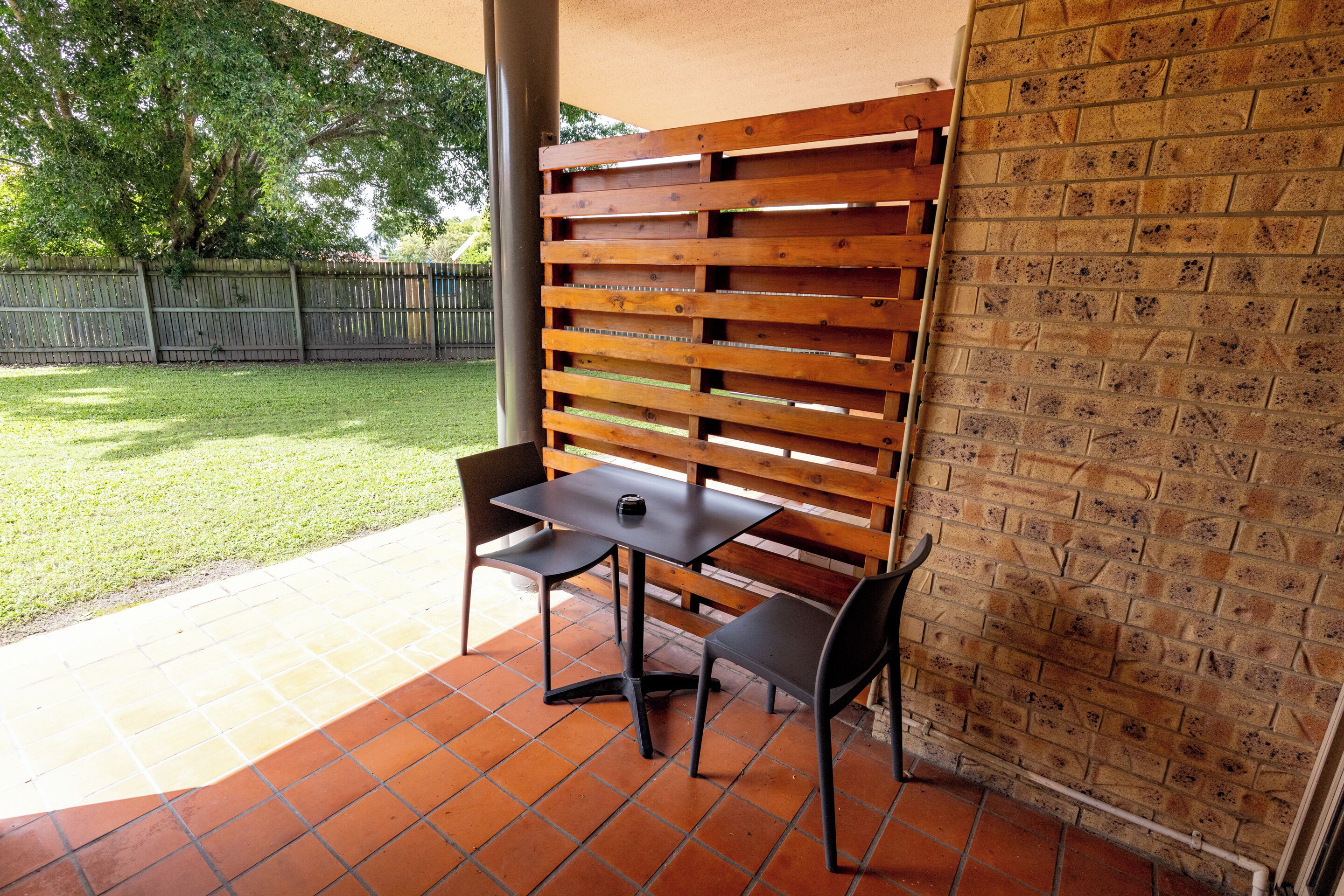 An outdoor patio area with a brick floor, a wooden slatted wall, and a table with two chairs.