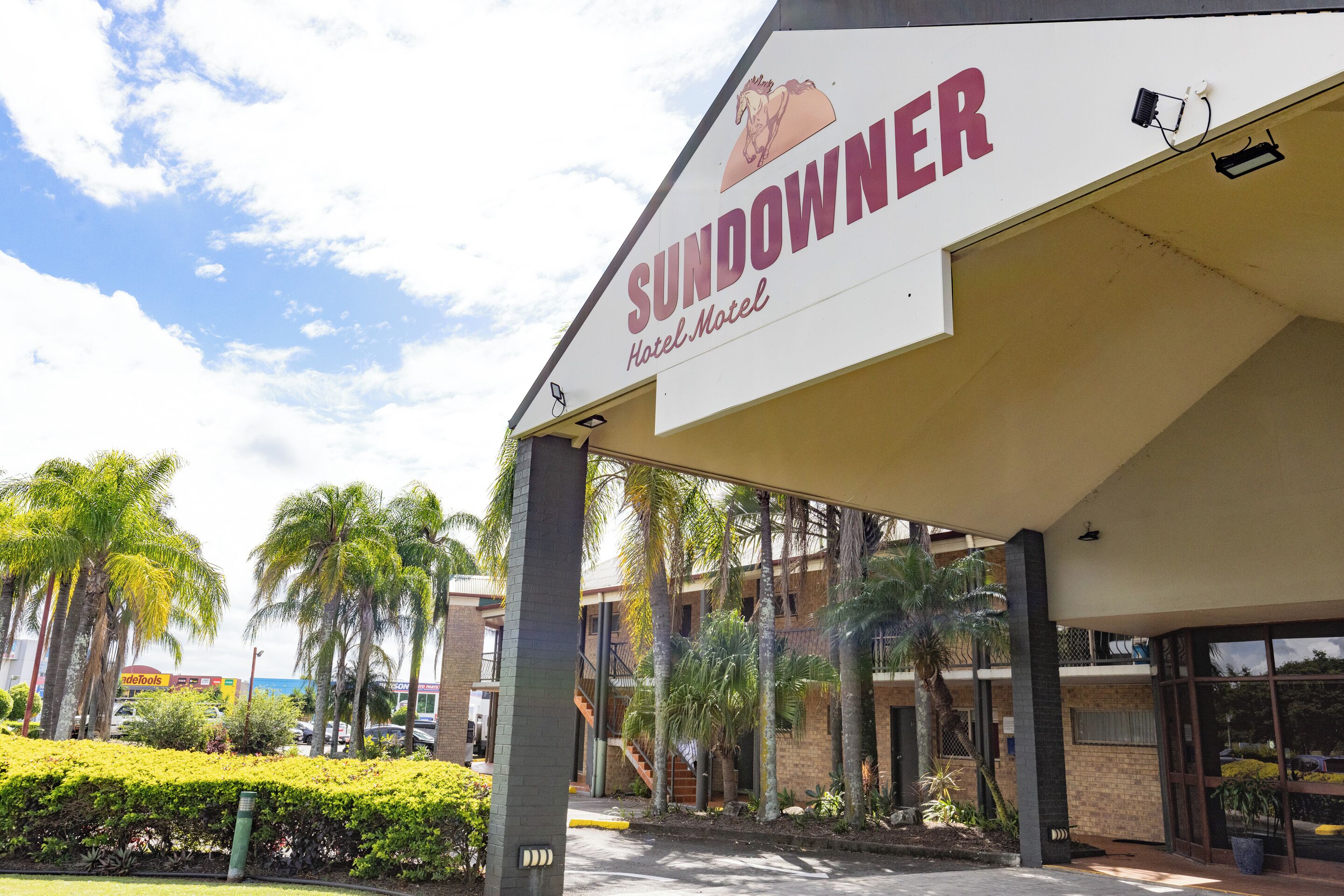 A hotel named 'Sundowner' with a covered entrance, palm trees, and a clear sky.