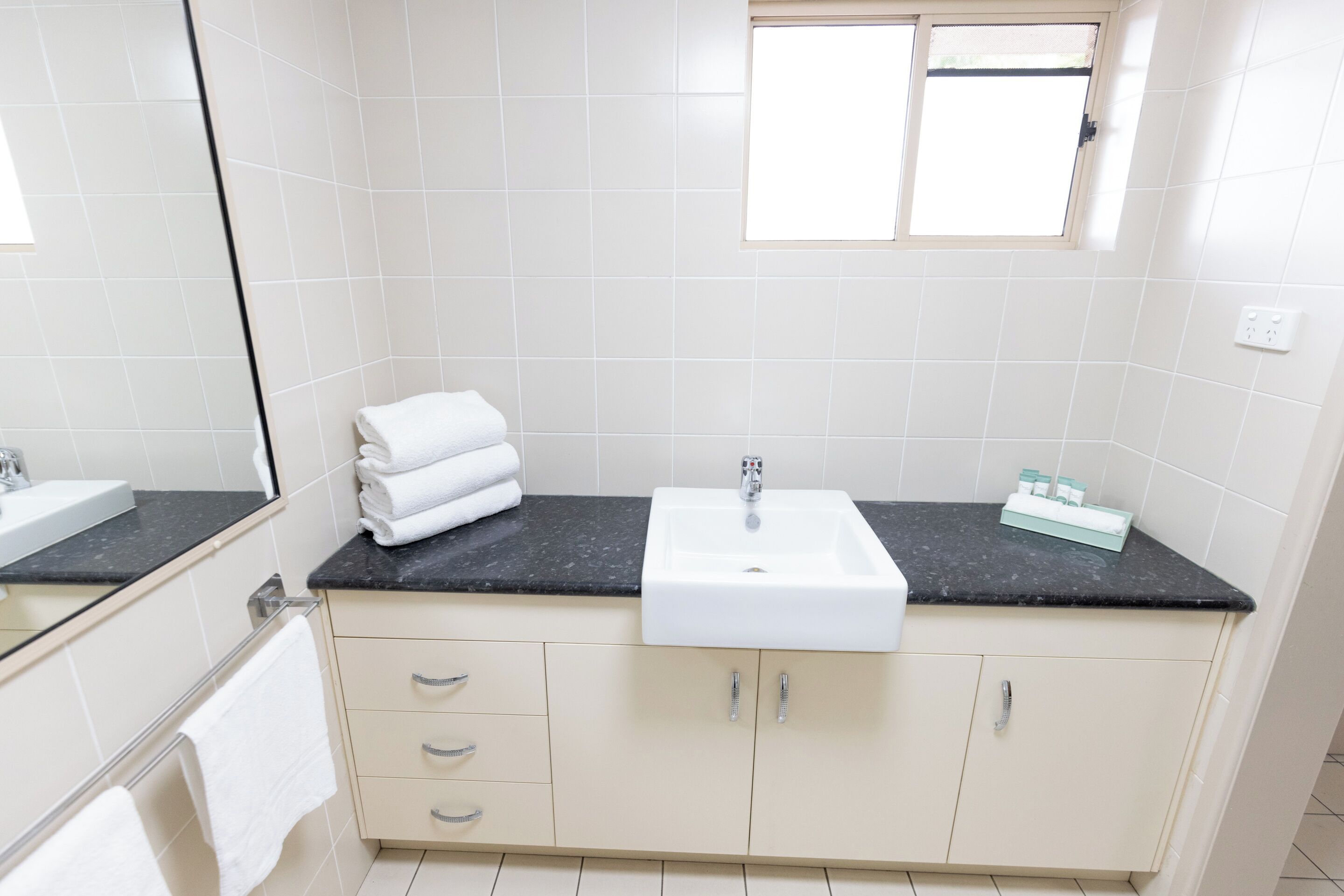 A bathroom with a white sink, beige cabinets, and a black countertop.