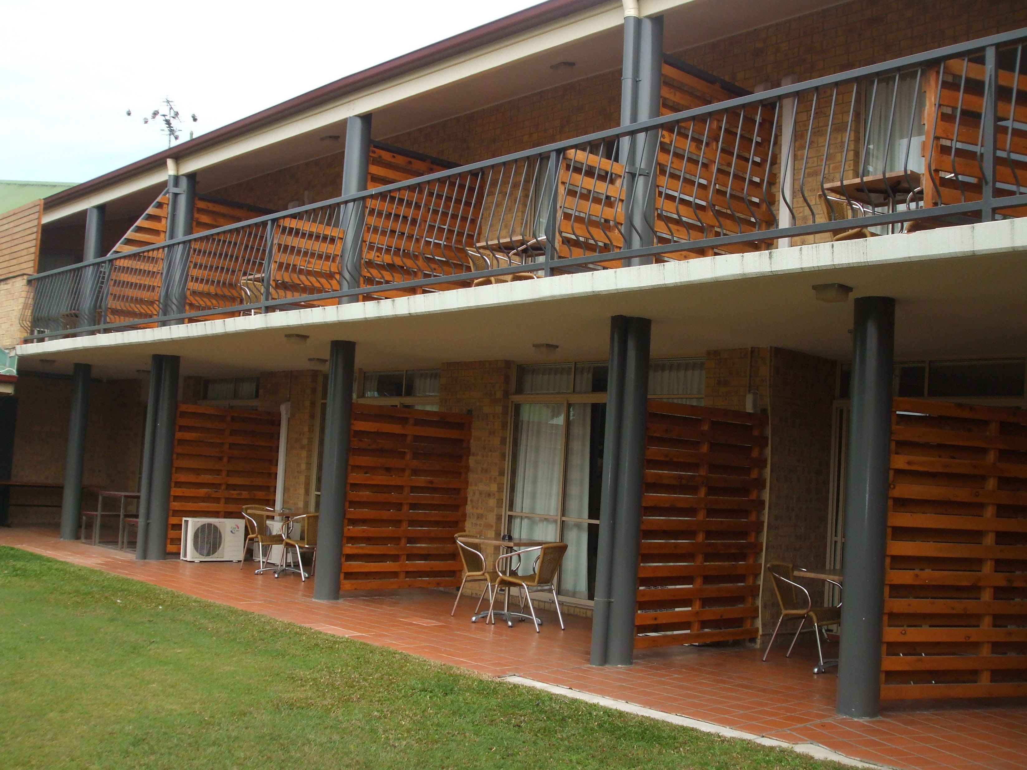 Un bâtiment moderne doté d’un espace extérieur couvert, agrémenté de lambris en bois, de garde-corps en métal et de sièges pour se détendre en plein air.