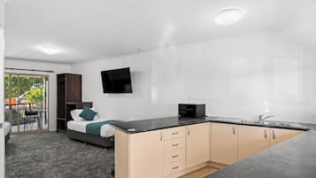 Una habitación moderna y funcional con cama, kitchenette y televisor montado en la pared.