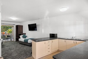 A modern, compact room with a bed, a kitchenette, and a TV mounted on the wall. - Sundowner Hotel Motel (Caboolture)