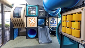 Une aire de jeux avec un toboggan, un espace réservé aux tout-petits et un panneau indiquant la sortie.