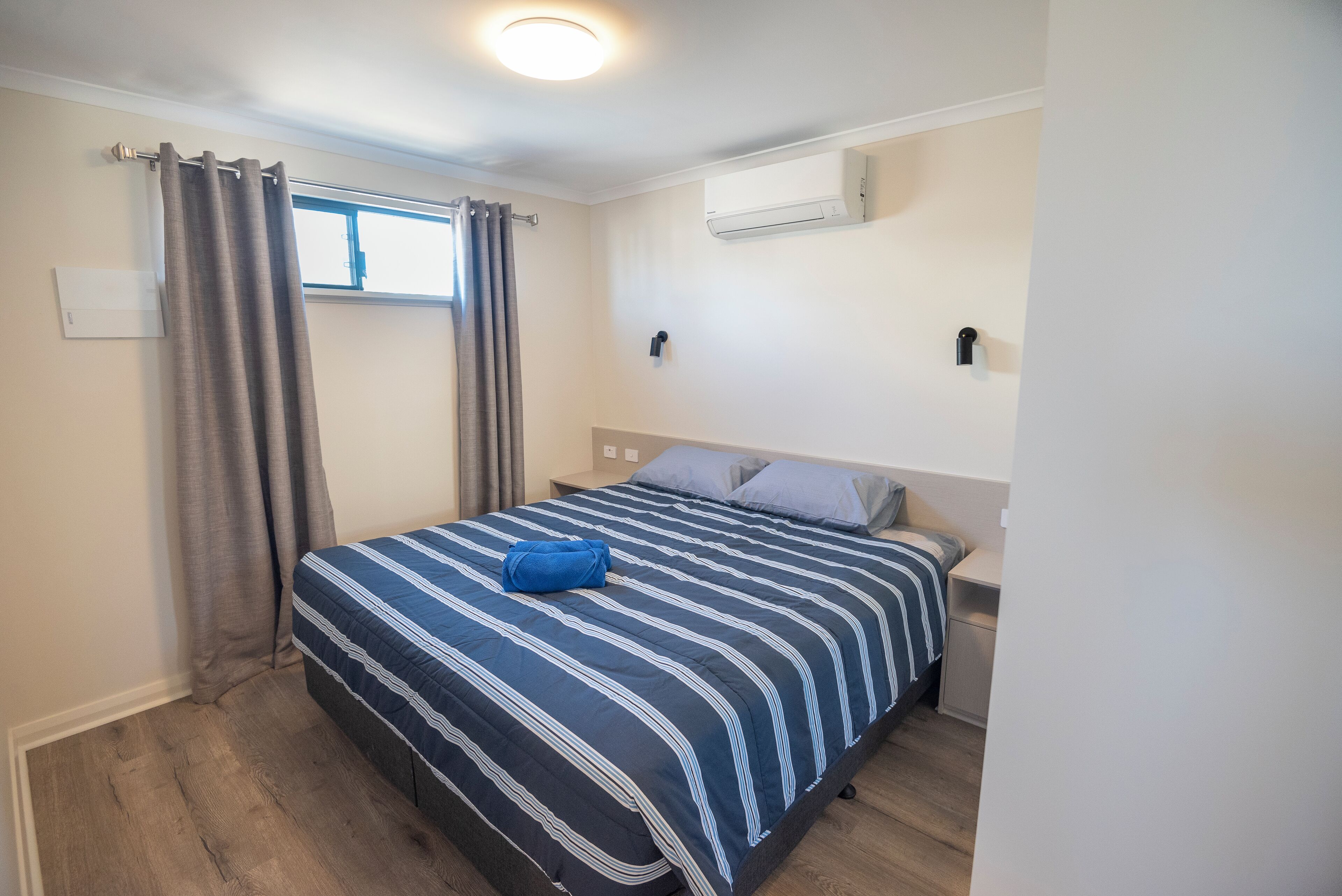 Un dormitorio con cama, cortinas, aire acondicionado y mesita de noche.