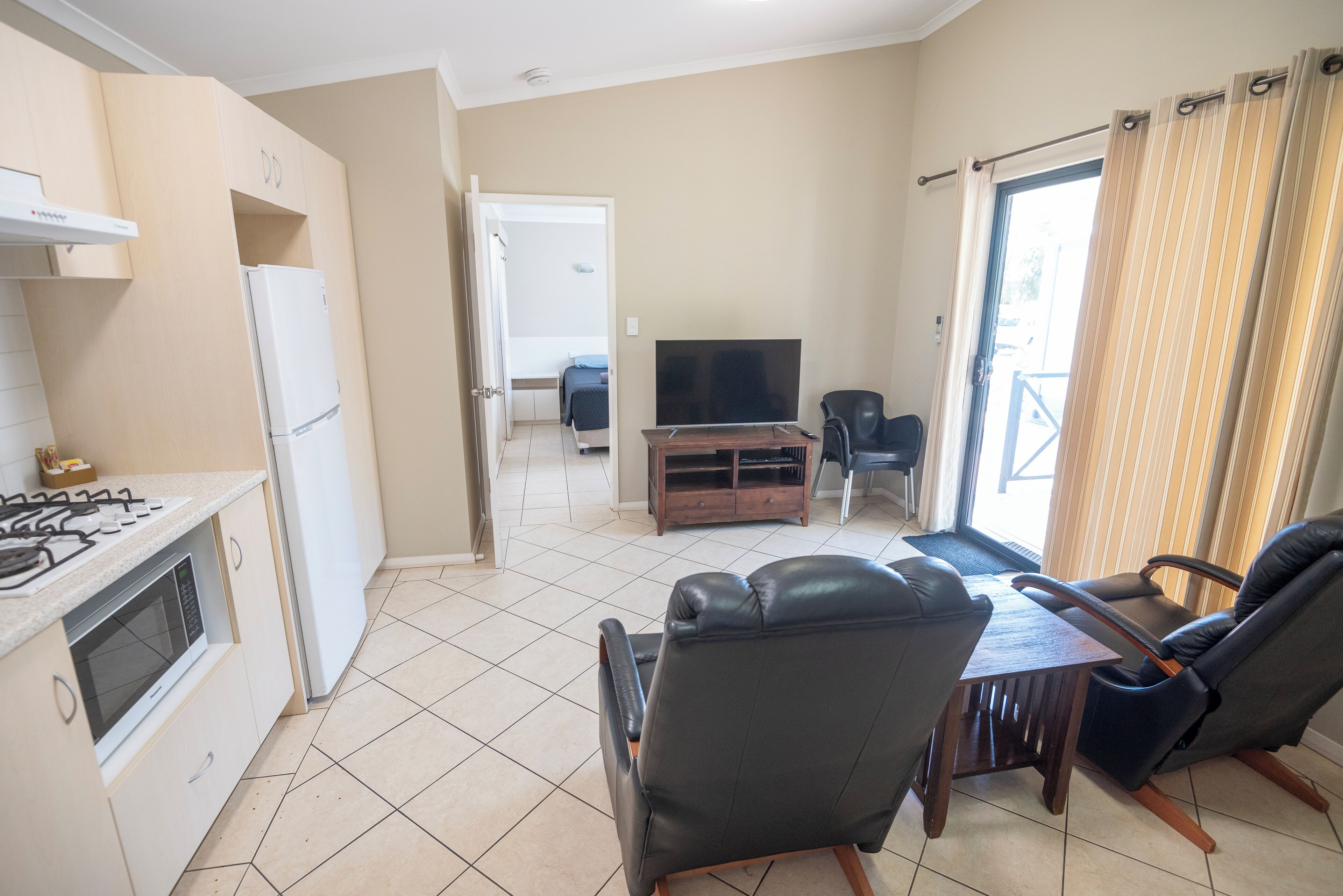 Een compacte woonruimte met een kitchenette, een eethoek met een tafel en stoelen, een televisie, en een schuifdeur die leidt naar een aangrenzende kamer.