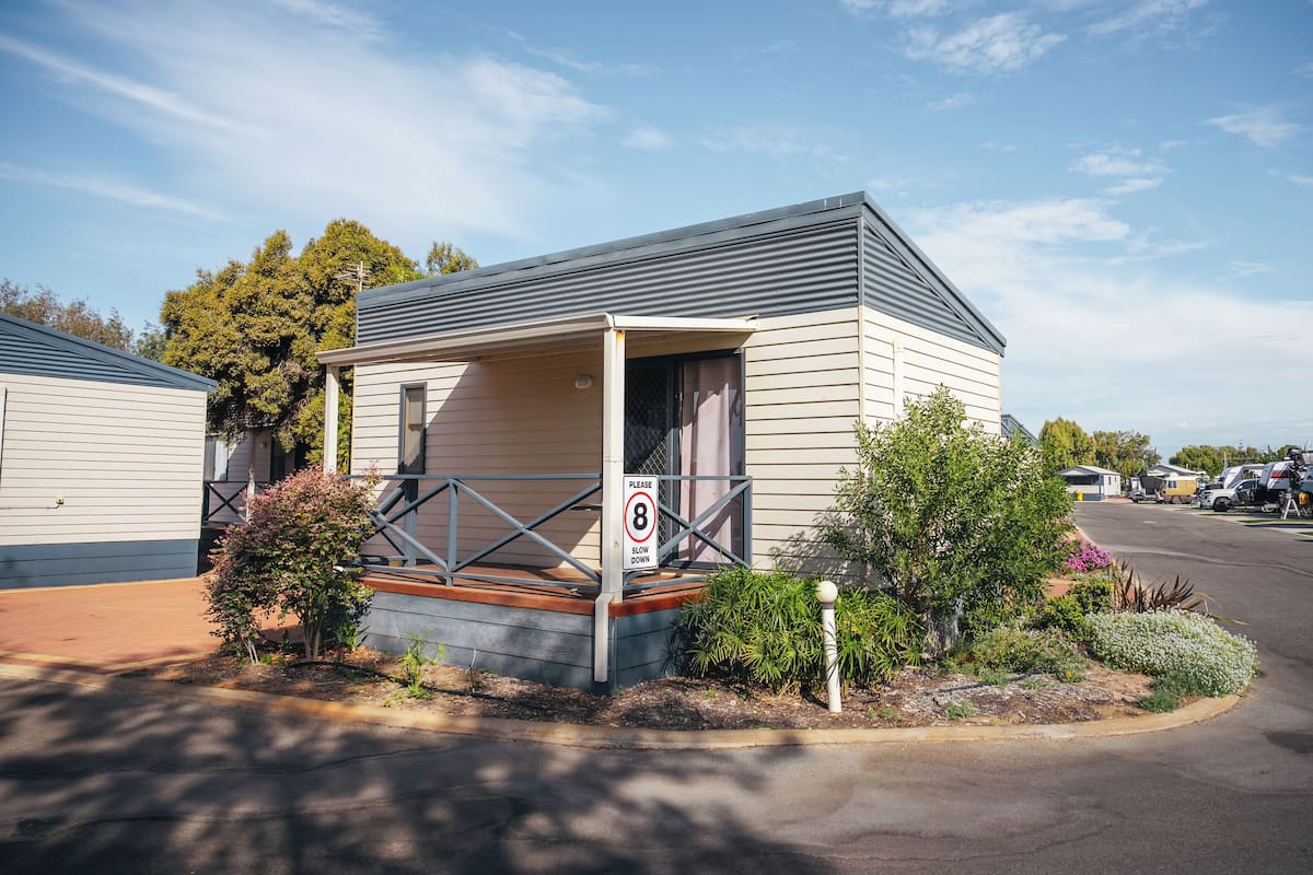 A single-story mobile home with a porch, a speed limit sign, and a parking area with RVs.