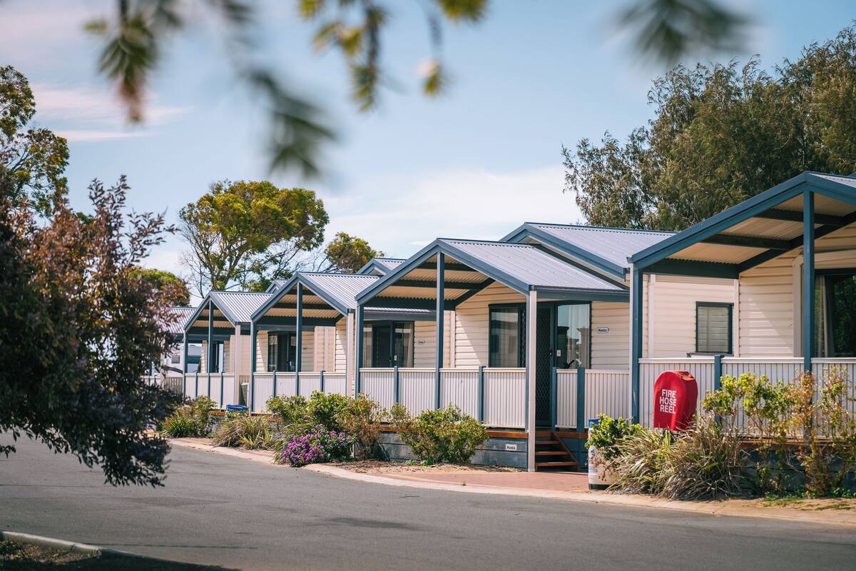 A row of mobile homes with metal roofs and white siding, each with a porch and a small garden area.