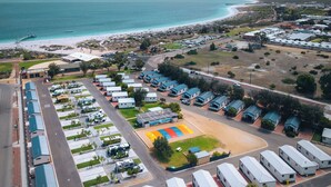 Une vue aérienne d’une station balnéaire comprenant de nombreux hébergements de type caravane, un terrain de sport central et une plage à proximité.
