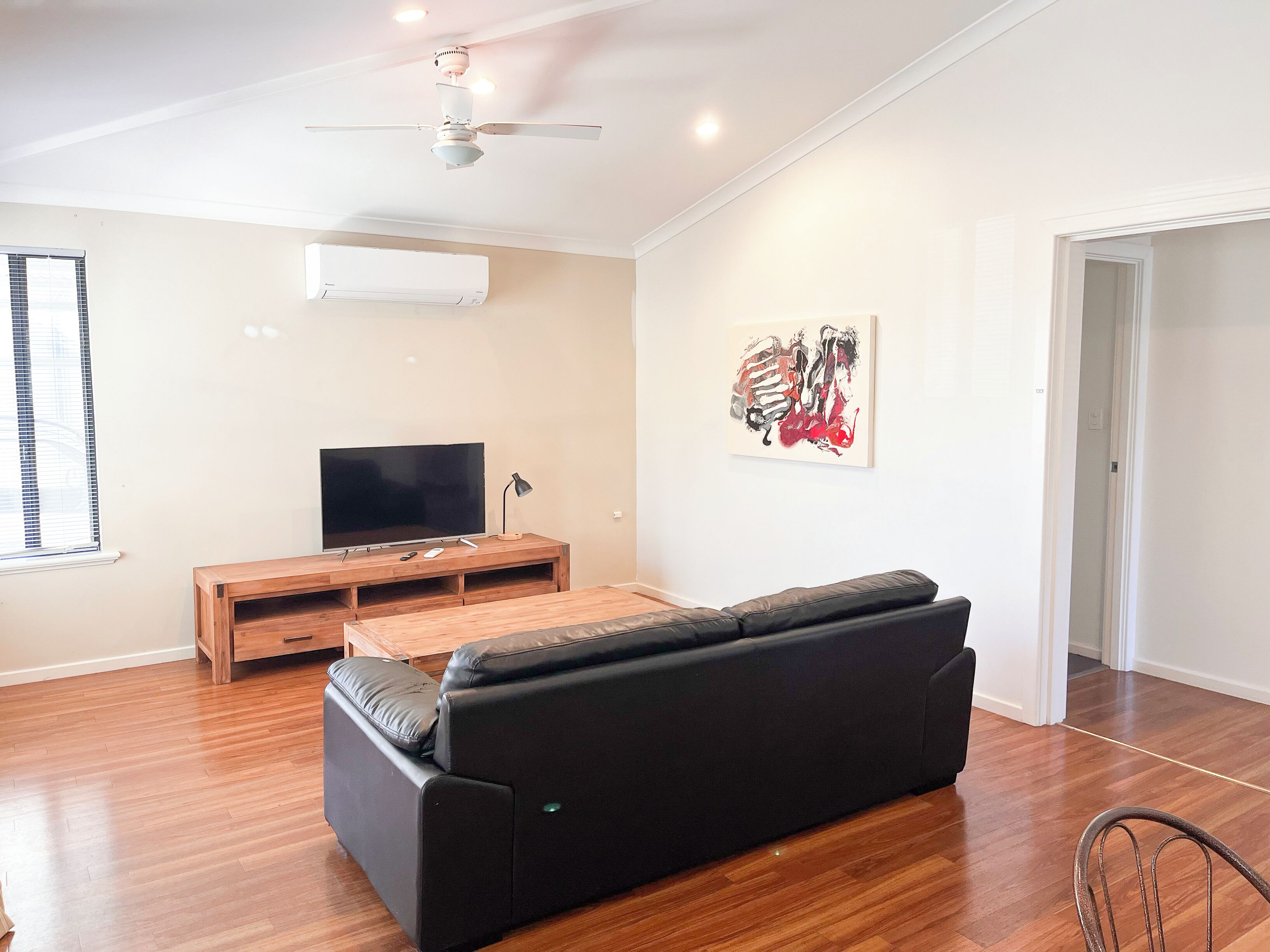 A modern living room with a black leather sofa, wooden coffee table, and a flat-screen TV on a wooden stand.