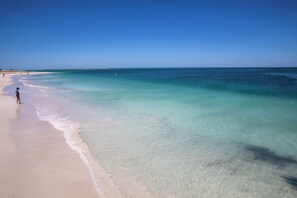 Une plage avec une eau turquoise et limpide, et une personne debout sur le sable.