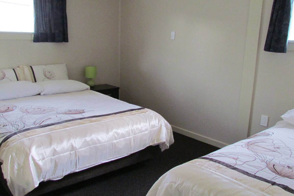 Habitación de hotel con dos camas, una mesita de noche y un ventanal con cortinas.