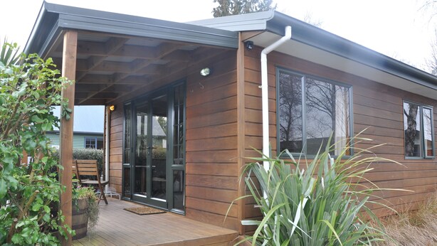 A modern wooden house with a covered porch, large windows, and a door leading to a garage. - Birchwood Cottages (Te Anau)