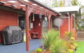 A covered patio area with a barbecue grill, a welcome sign, and potted plants. - Birchwood Cottages (Te Anau)