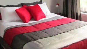 A bed with a red and grey bedspread, white pillows, and a red rose painting on the wall. - Birchwood Cottages (Te Anau)