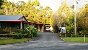 A building with a red roof and a covered entrance, surrounded by greenery and trees. - The Crays Accommodation (Strahan)