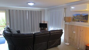 A living room with a black leather sofa, a flat-screen TV on a stand, and a painting on the wall. - The Crays Accommodation (Strahan)