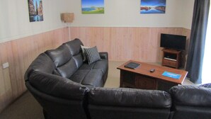 A living room with a leather sofa, a small wooden table, a flat-screen TV, and three wall-mounted paintings. - The Crays Accommodation (Strahan)