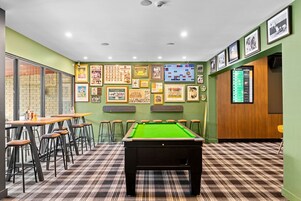 Una sala de billar con mesa de pool, taburetes y cuadros en las paredes.