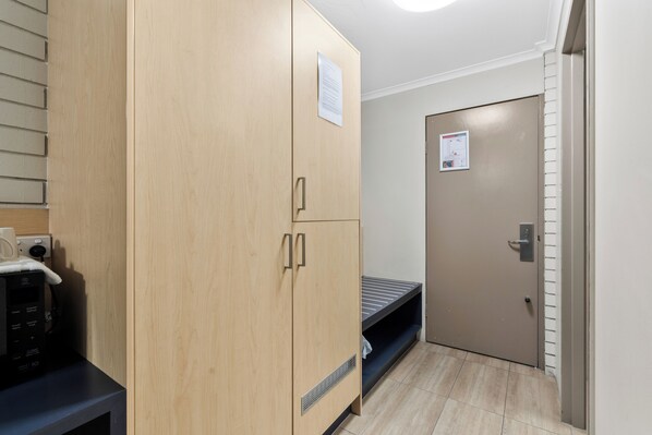 A room with a wooden wardrobe, a microwave, a bed, and a door with a notice. - Morayfield Tavern & Motel (Caboolture South)