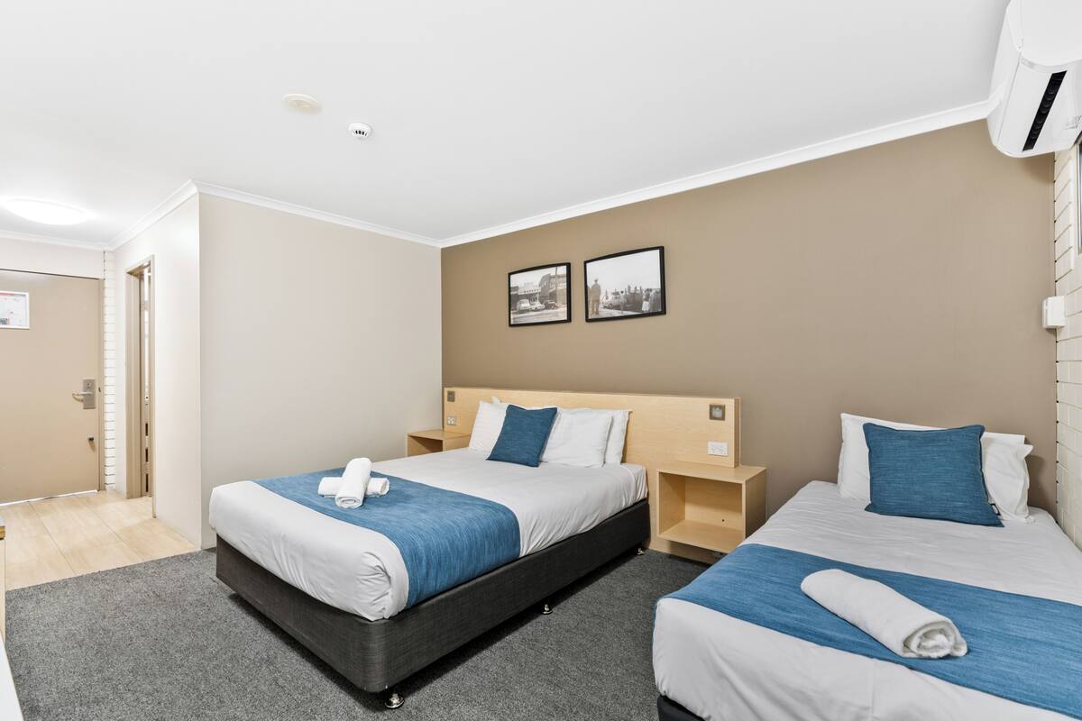 A hotel room with two beds, a grey carpet, beige walls, and a white ceiling.