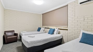 A hotel room with two beds, a brown armchair, and a window with blinds.