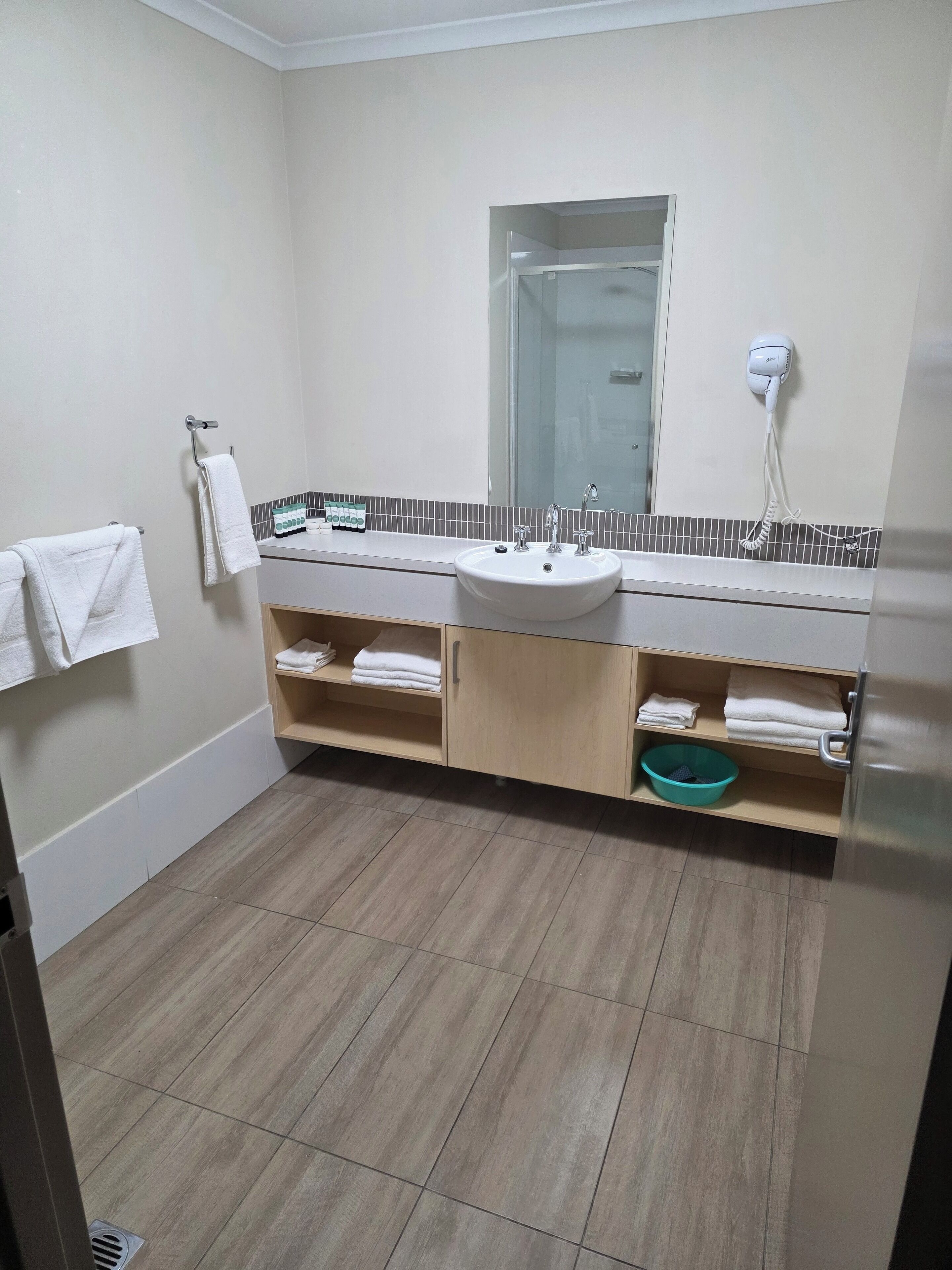 Een badkamer met een wastafel, spiegel, handdoekrek en planken met opgevouwen handdoeken.