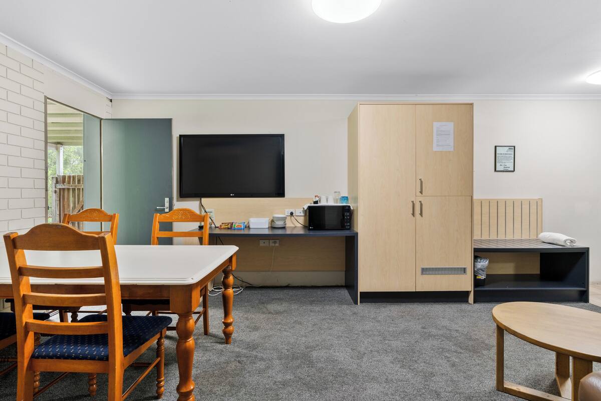 A small, well-lit room with a wooden table and chairs, a flat-screen TV, a microwave, and a cabinet.