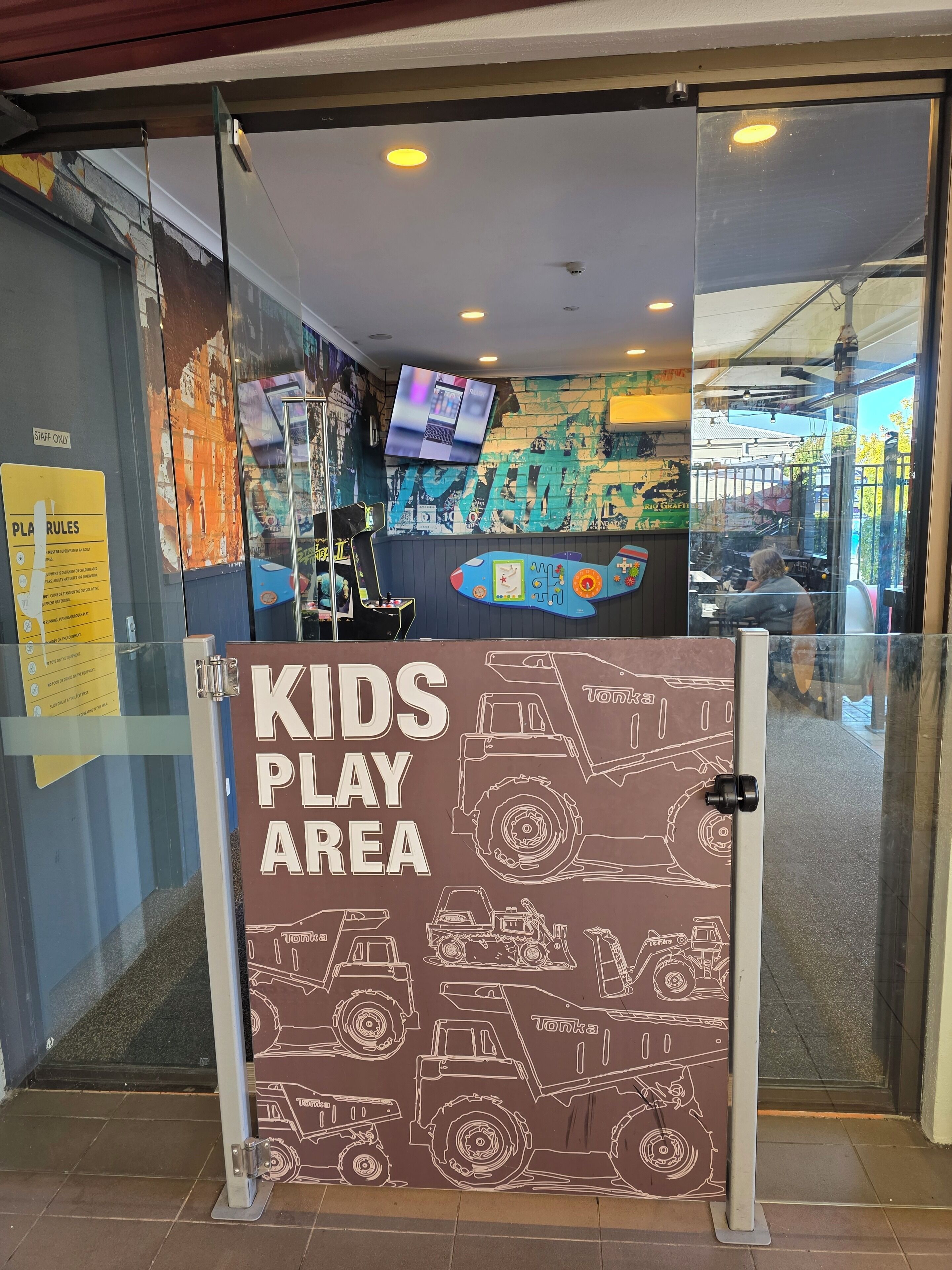 Une entrée avec une porte en verre, sur laquelle on peut lire les inscriptions suivantes : « ESPACE DE JEUX POUR ENFANTS », « RÉSERVÉ AU PERSONNEL » et « RÈGLES DU JEU ».