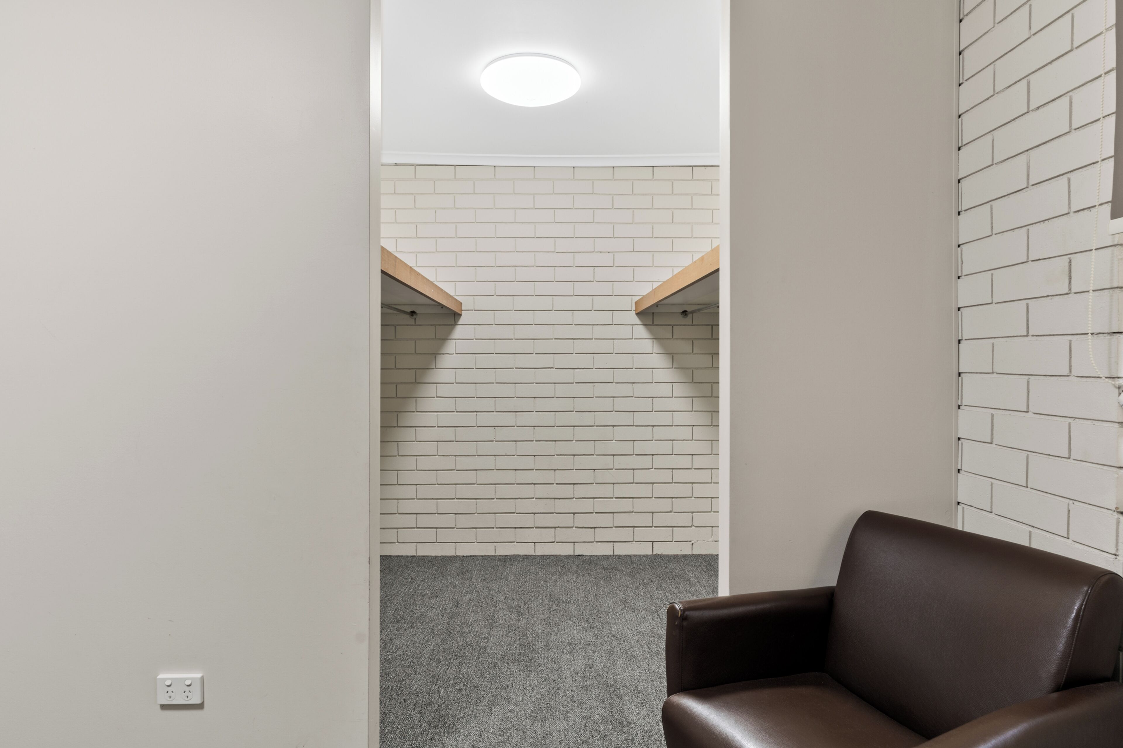 A modern room with a brown leather chair, white brick walls, and a grey carpet.