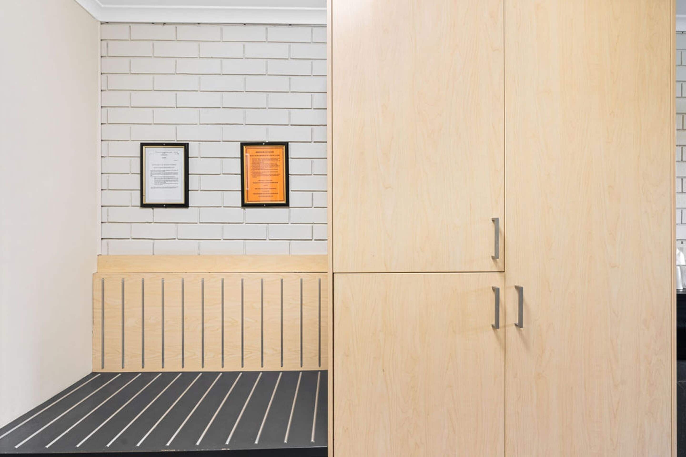 Une pièce comprenant un lit, une armoire en bois et deux documents encadrés accrochés à un mur en briques.