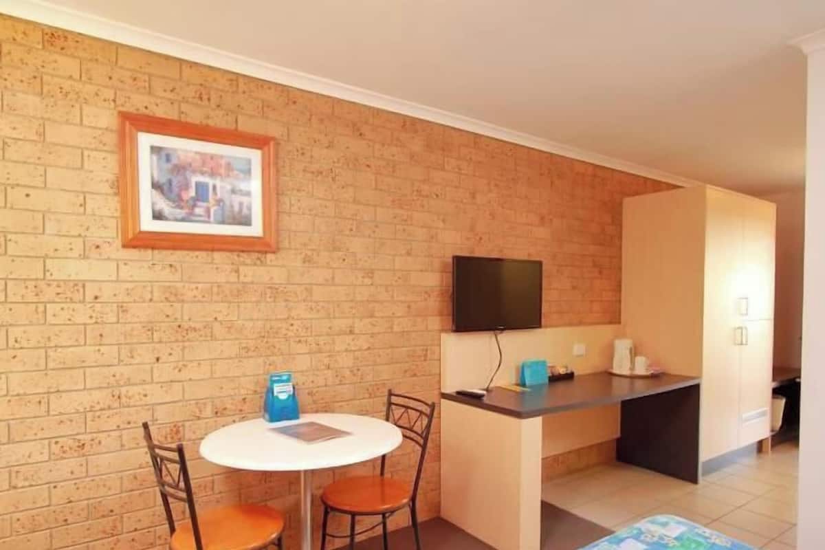 A small room with a brick wall, a television mounted above a counter, and two chairs around a small table.