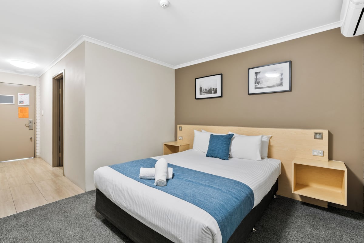 A hotel room with a large bed, two nightstands, a wooden headboard, and two framed pictures on the wall.