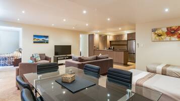 Una sala de estar moderna con una mesa de comedor de vidrio, sofás y una zona de cocina con refrigerador y estufa.