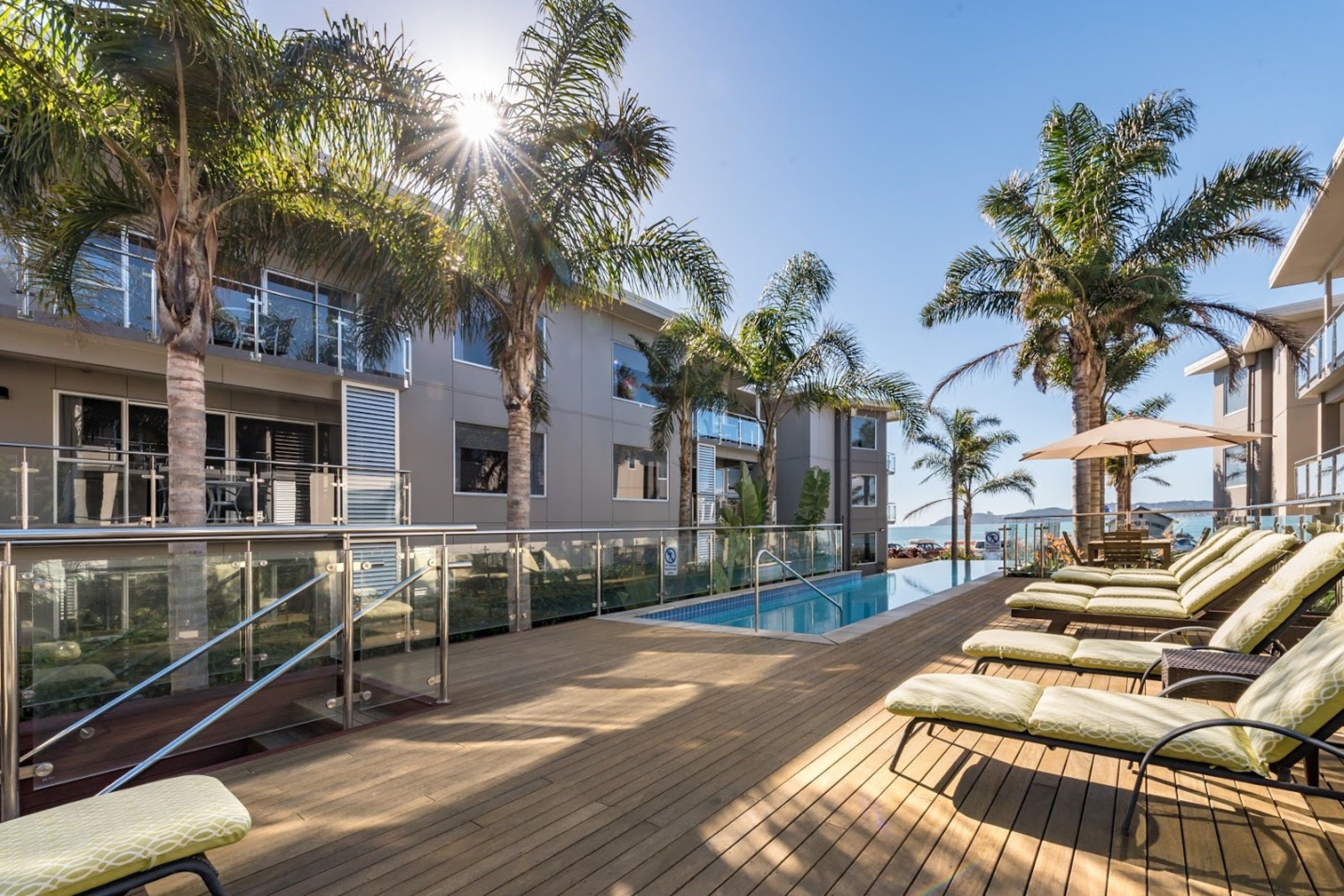A poolside area with lounge chairs, palm trees, and a clear view of the ocean.