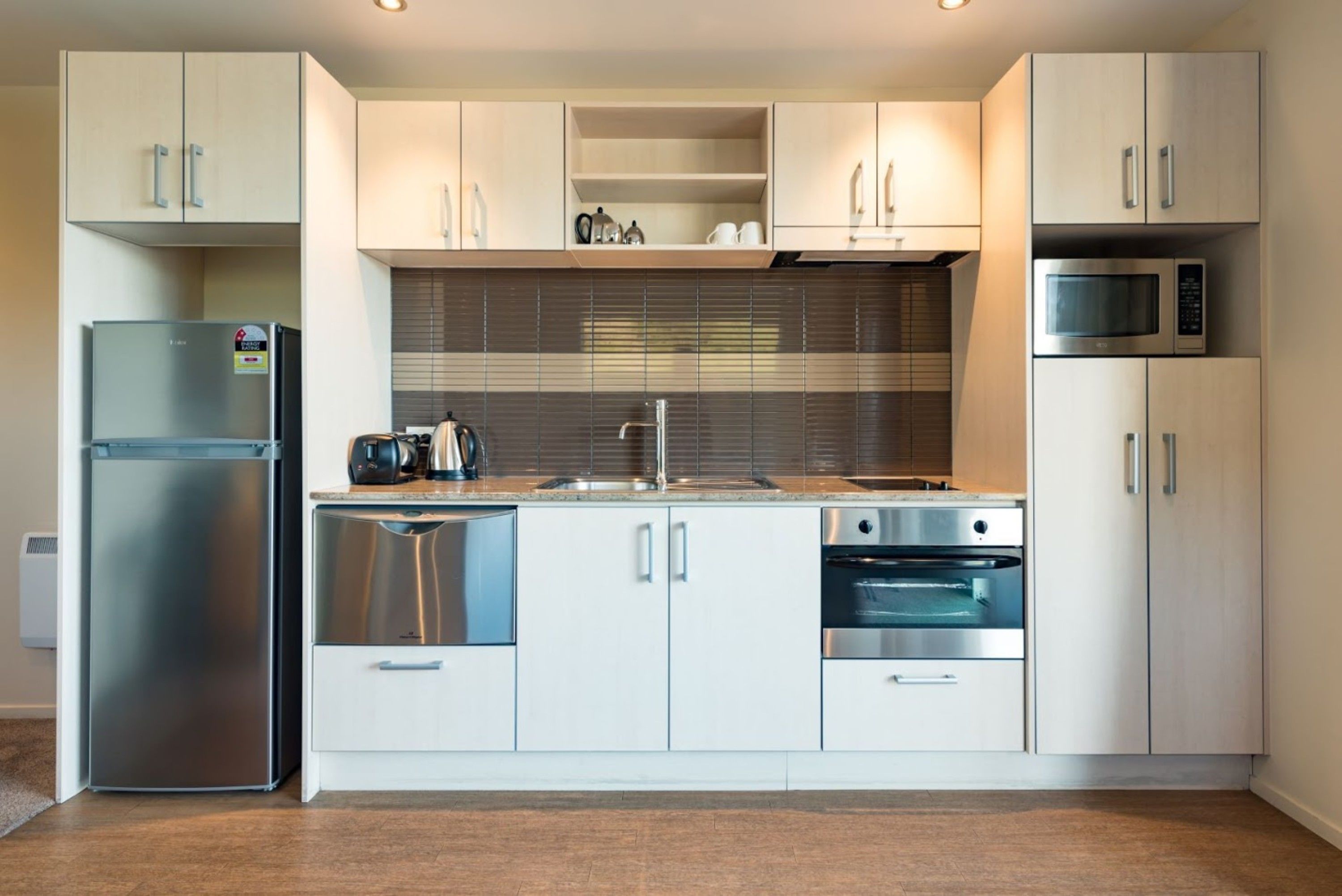 A modern kitchen with stainless steel appliances, white cabinetry, and a tiled backsplash.