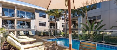 A poolside area with lounge chairs, a wooden deck, and a pool.