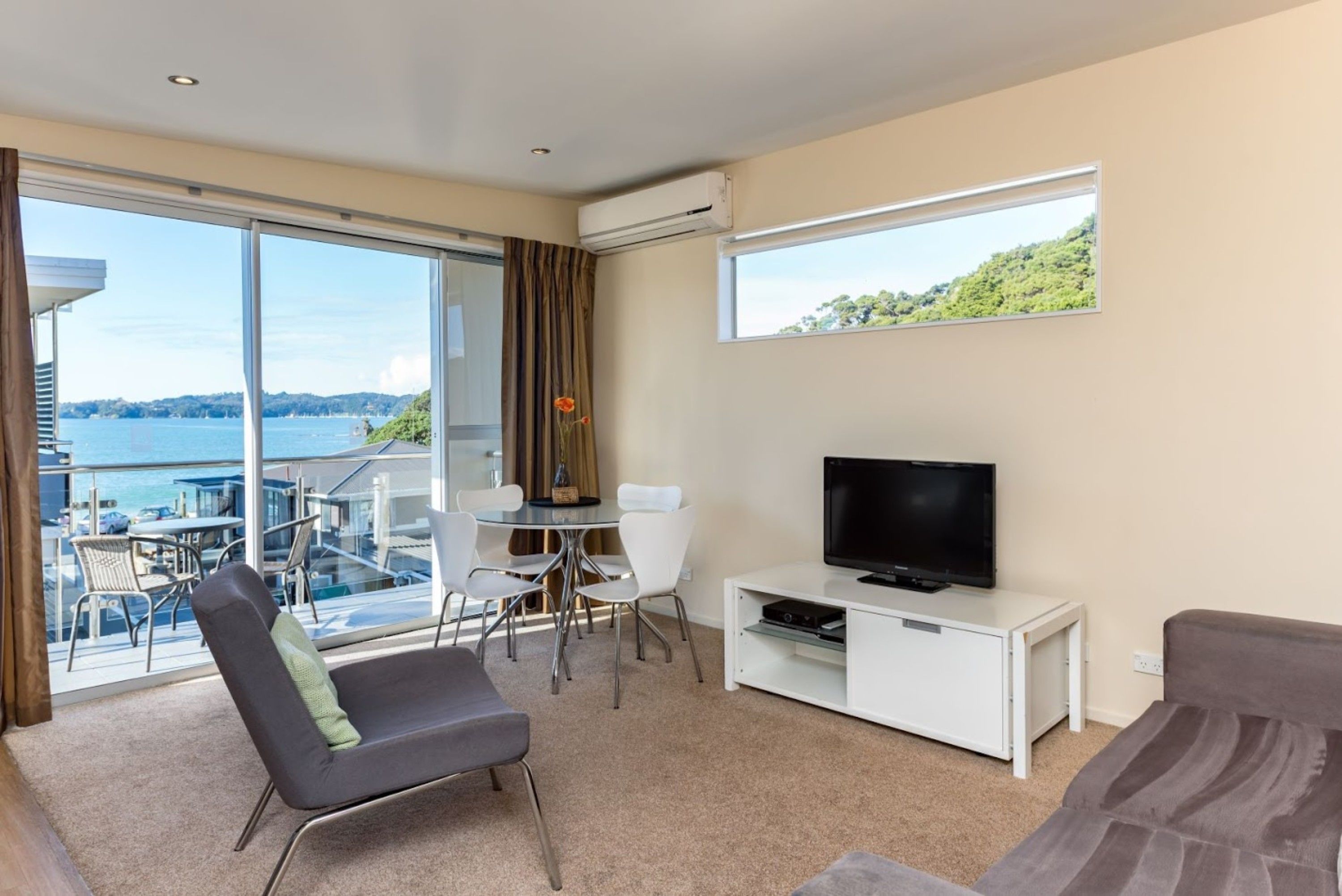 Een moderne hotelkamer met balkon, een flatscreen-tv en een eethoek met witte stoelen.