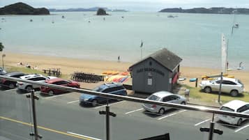 A view of a beach with a small building labeled "Bay Beach Hire" and several parked cars along the roadside.