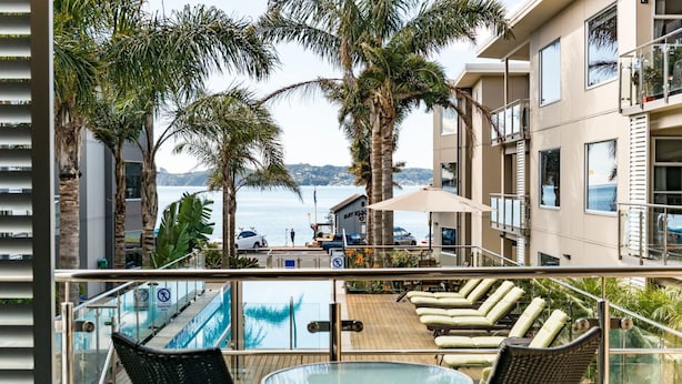 A balcony with a pool view, lounge chairs, and a table. - Edgewater Palms Apartments (Paihia)
