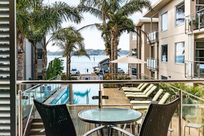 Un balcón con vista a la piscina, sillones de descanso y una mesa.