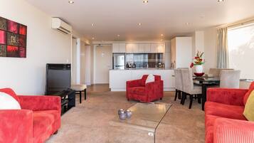 Una sala de estar moderna con sofás rojos, una mesa de centro de vidrio y una cocina al fondo.