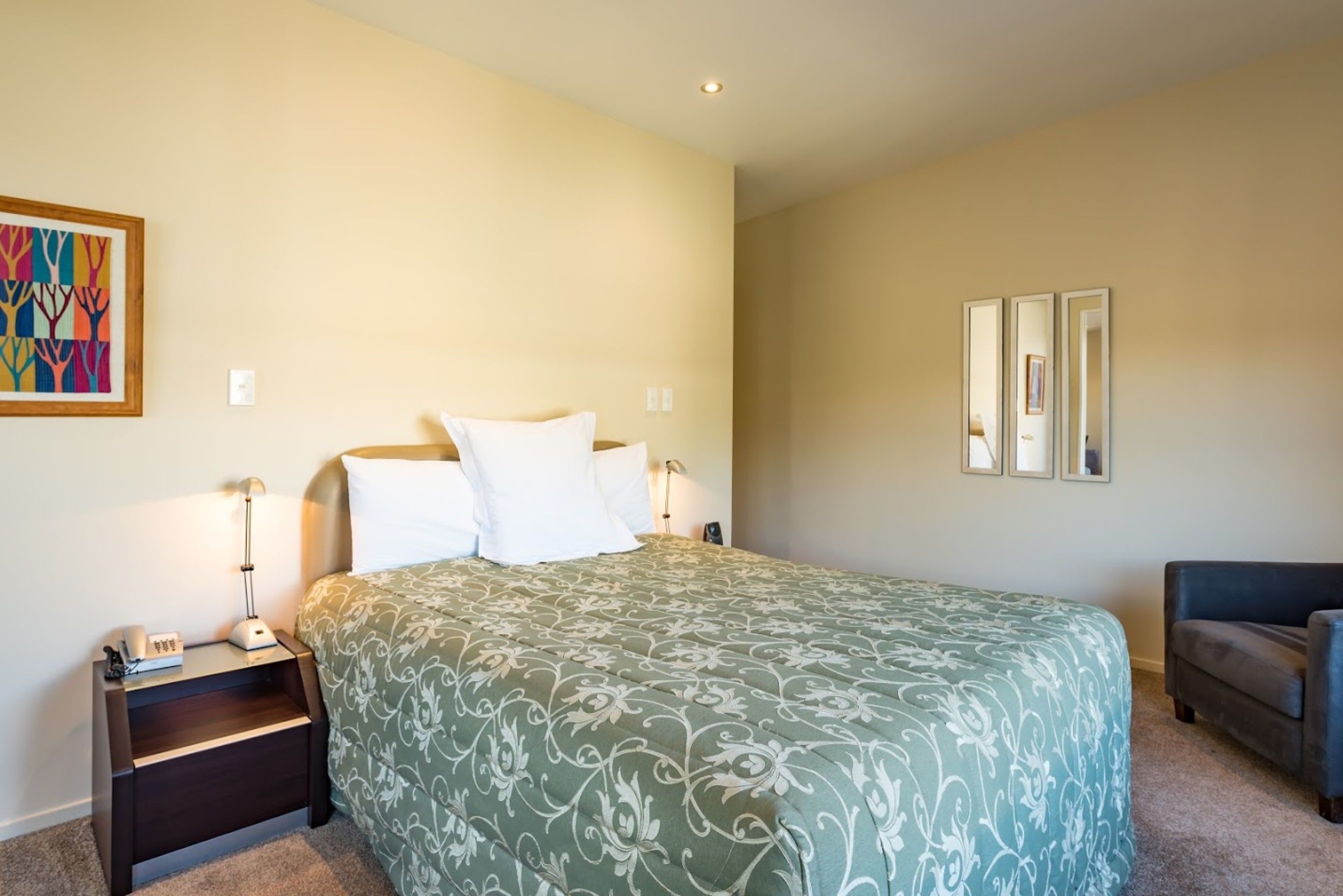 A bedroom with a bed, nightstands, a lamp, a chair, and a framed picture on the wall.