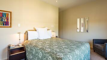 A bedroom with a bed, nightstands, a lamp, a chair, and a framed picture on the wall.