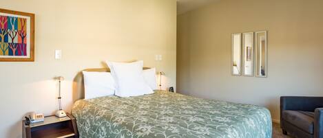 A bedroom with a bed, nightstands, a lamp, a chair, and a framed picture on the wall.