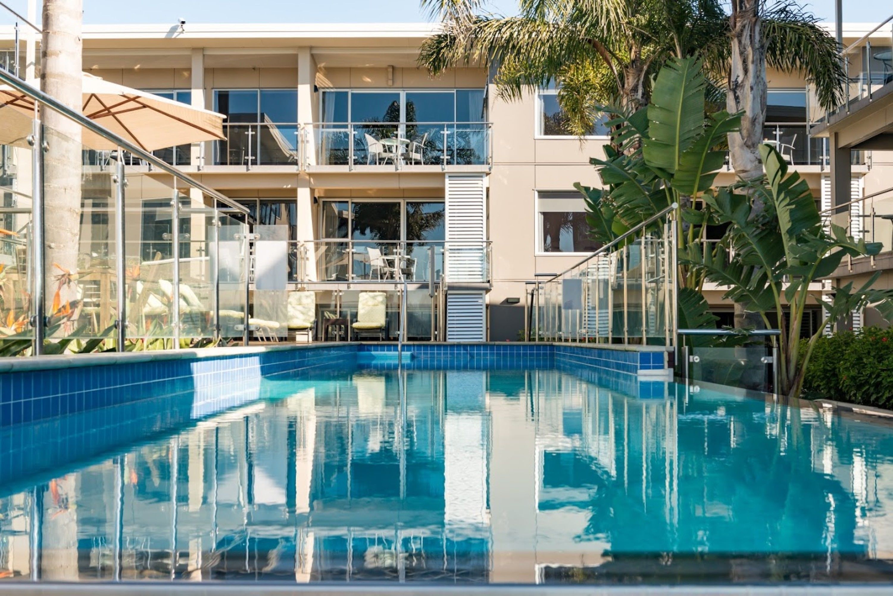 An indoor swimming pool with clear blue water, surrounded by glass railings and a modern building with balconies.