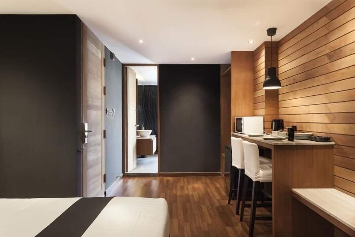 Una habitación de hotel moderna con cama, escritorio y una silla. Tiene una pared de madera y una puerta de color oscuro.