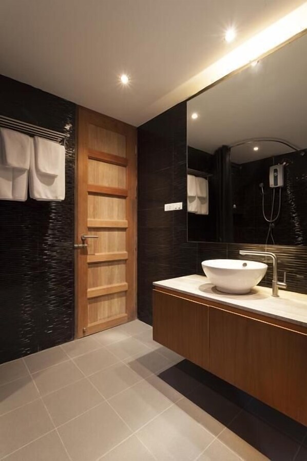 A modern bathroom with a wooden door, a large mirror, a white sink, and a dark tiled wall. - 5ive Beach House Hotel (Pattaya)