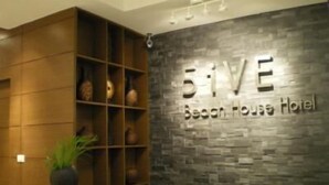 A reception desk with a wooden panel design and a stone wall with the name "5ive Beach House Hotel" in the background. - 5ive Beach House Hotel (Pattaya)
